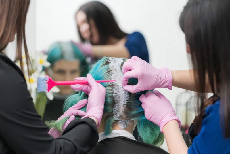 process-of-hair-dyeing-in-beauty-salon-two-hairdressers-apply-paint-to-hair-during-bleaching-hair